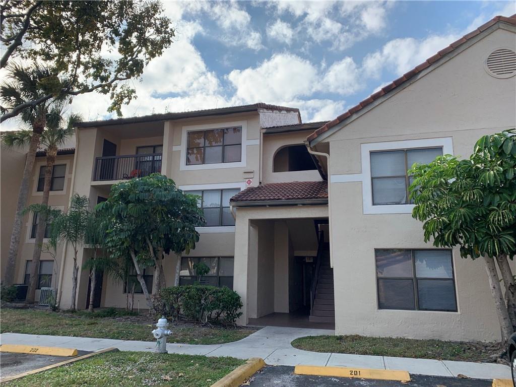 A multi-story apartment building exterior features tan stucco walls, a tiled roof, and parking spaces — 4341 W Mcnab Road # 22, Pompano Beach FL 33069, POMPANO BEACH, FL
