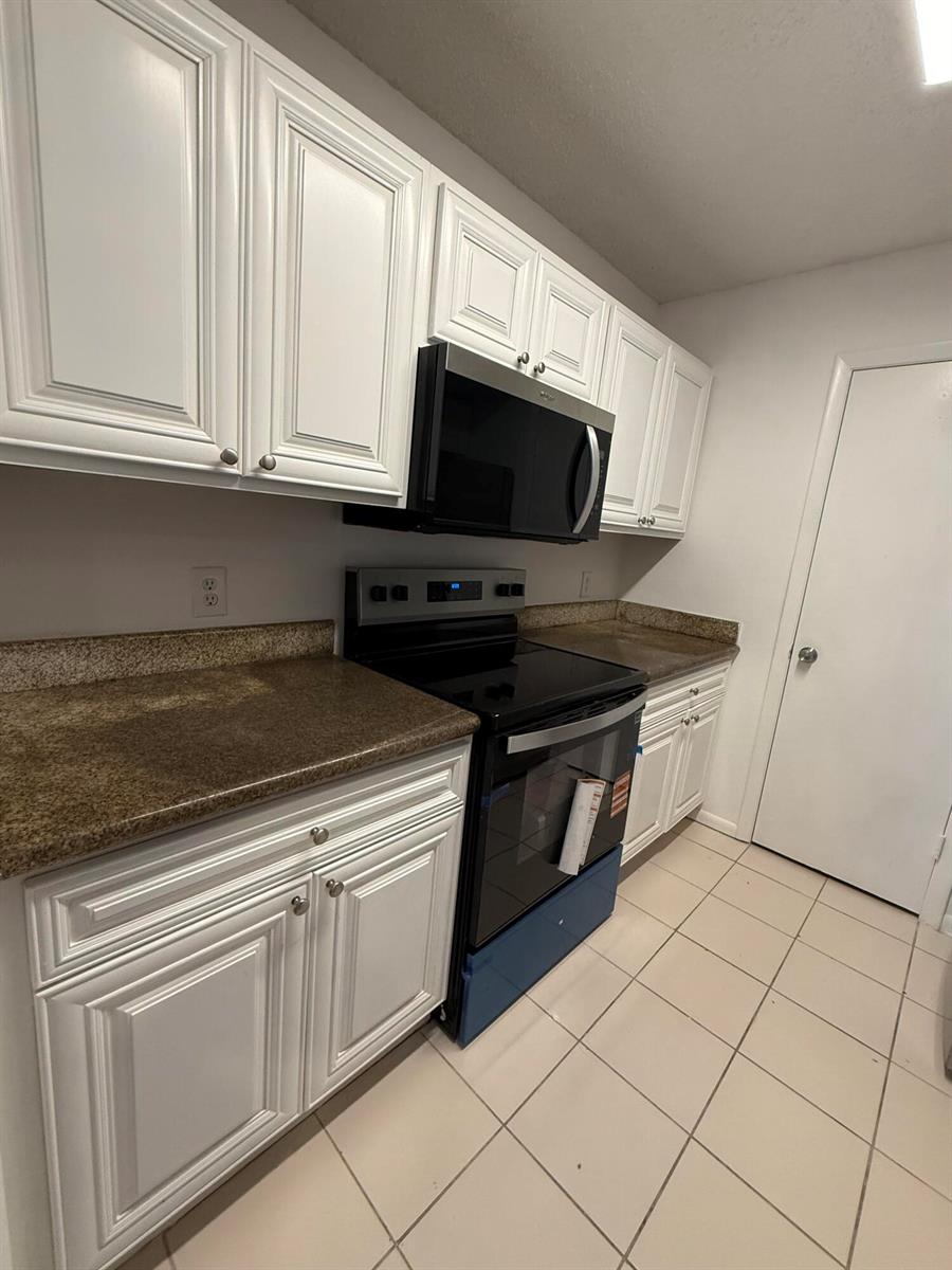 A kitchen features white cabinets, granite countertops, and black appliances over a tiled floor — 4341 W Mcnab Road # 22, Pompano Beach FL 33069, POMPANO BEACH, FL
