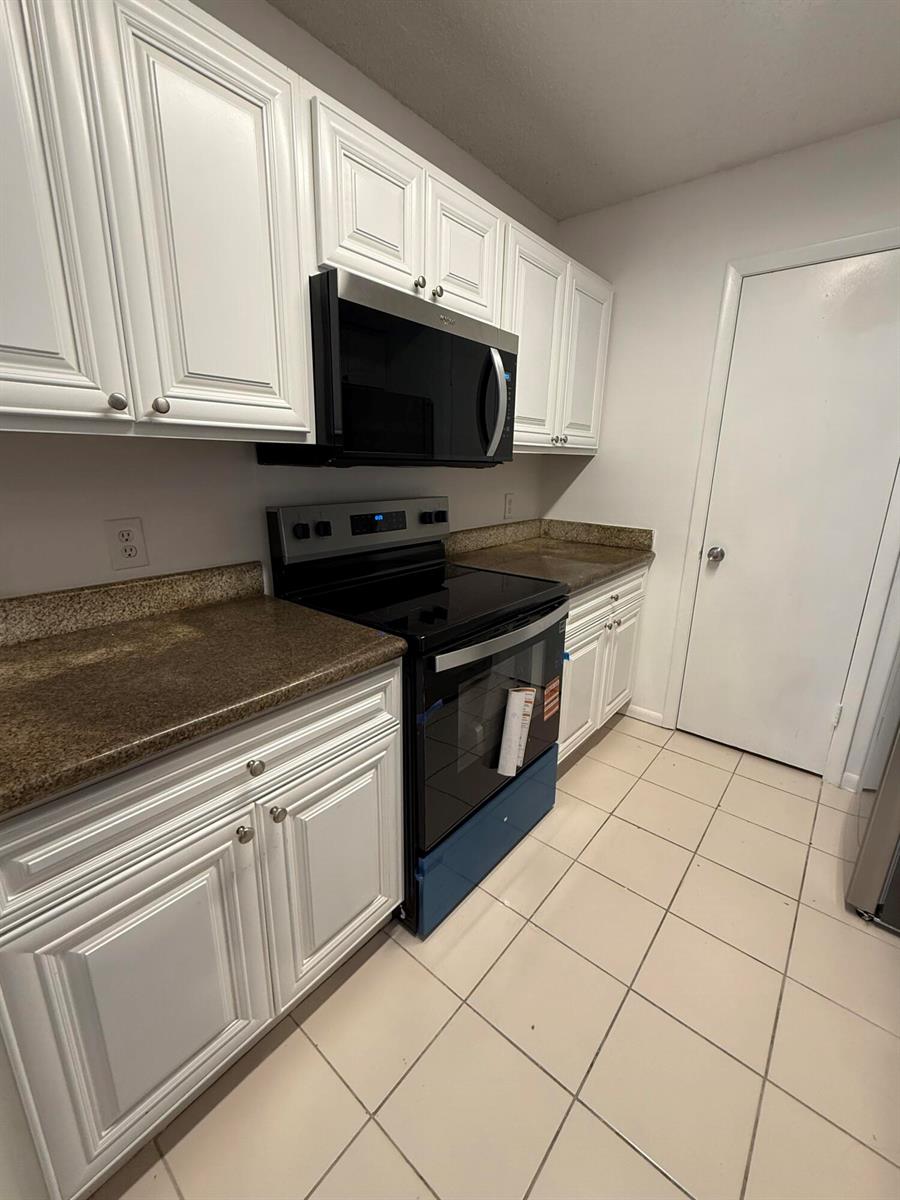 A kitchen features white cabinets, a black microwave and range, and brown granite countertops — 4341 W Mcnab Road # 22, Pompano Beach FL 33069, POMPANO BEACH, FL