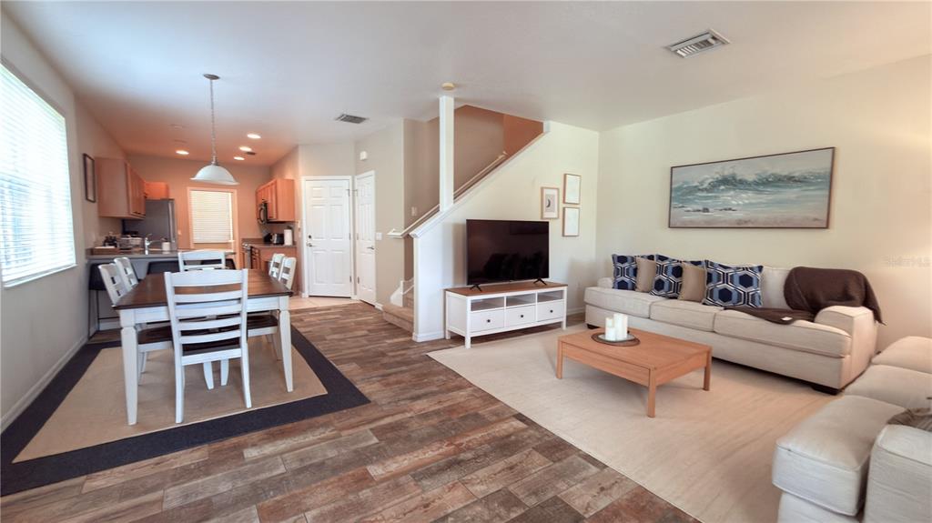 An open-concept living and dining area features wood-look tile flooring, a staircase, and neutral furniture — 3880 82ND AVENUE CIRCLE E UNIT 101, SARASOTA, FL