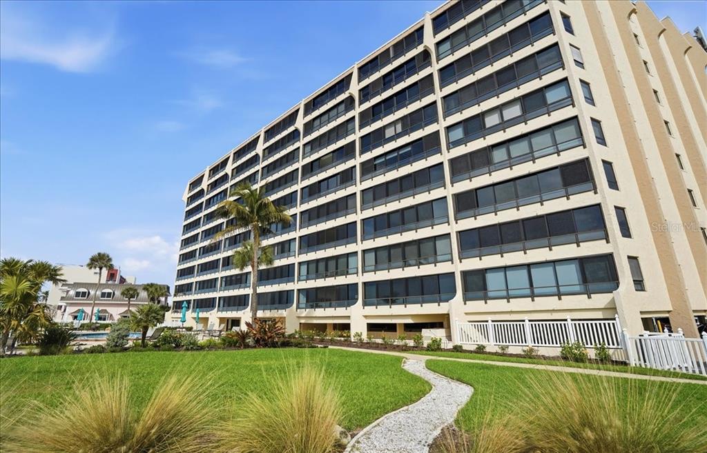 A multi-story apartment building stands next to a grassy lawn with a gravel path — 840 THE ESPLANADE N UNIT 206, VENICE, FL
