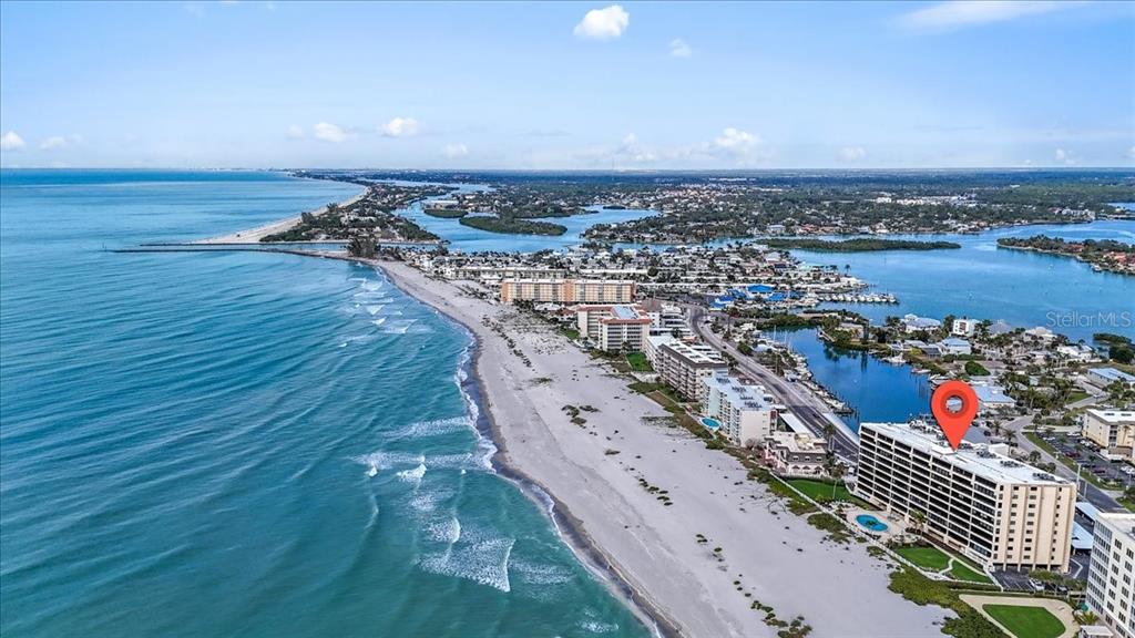 An aerial view shows a multi-story beachfront condominium building with a pool along the coast — 840 THE ESPLANADE N UNIT 206, VENICE, FL