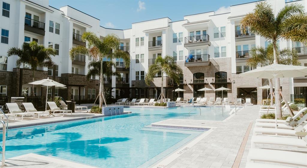A modern apartment complex courtyard featuring a swimming pool, lounge chairs, and palm trees — 700 AULTMAN STREET UNIT Broadway, KISSIMMEE, FL