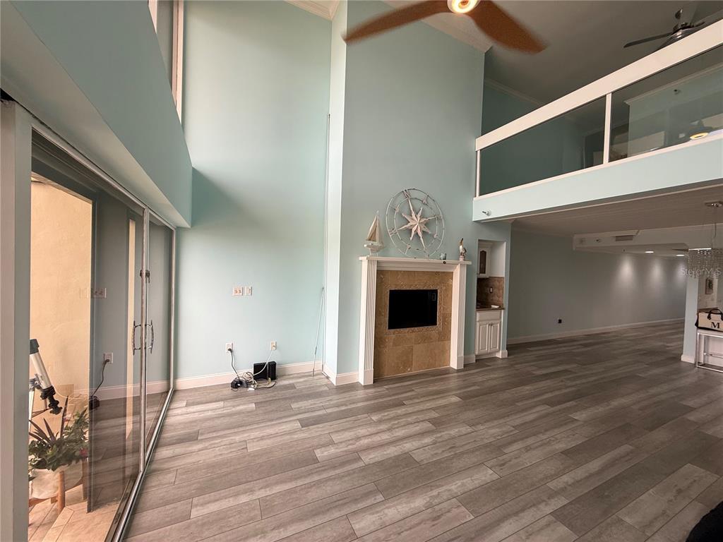 A living room with high ceilings, a fireplace, light wood floors, and a loft area — 19700 GULF BOULEVARD UNIT 202, INDIAN SHORES, FL