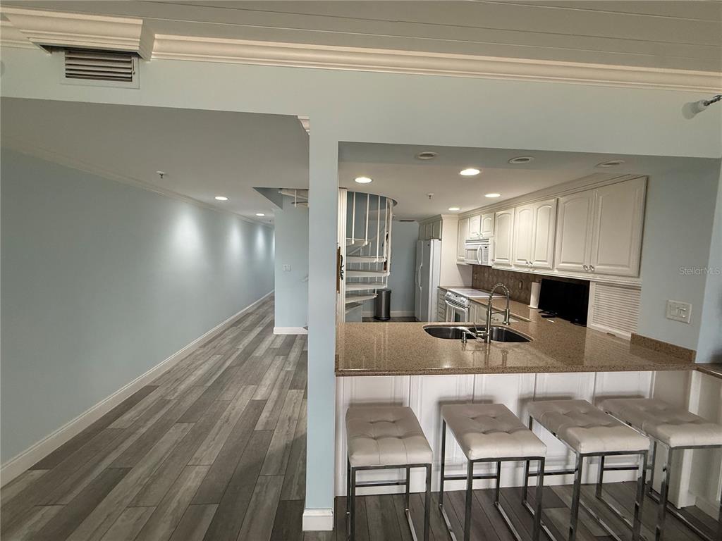 A kitchen with granite countertops and bar seating overlooks a long hallway with wood flooring — 19700 GULF BOULEVARD UNIT 202, INDIAN SHORES, FL