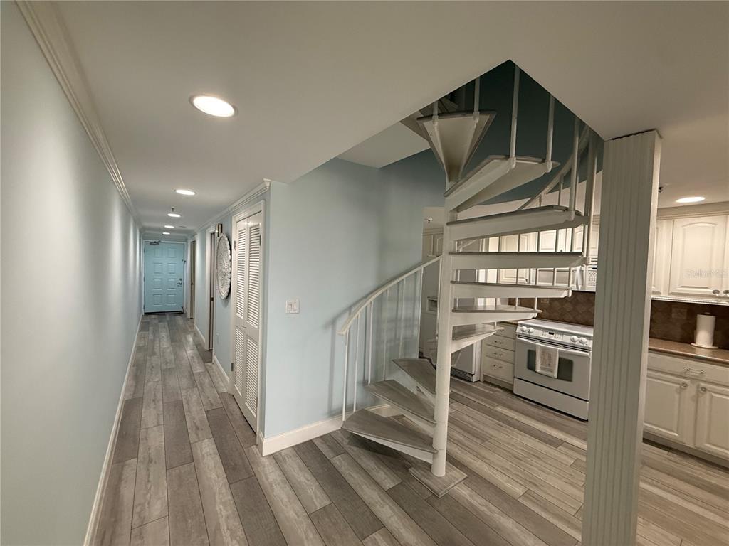 A hallway with light blue walls and wood-look flooring leads to a white spiral staircase — 19700 GULF BOULEVARD UNIT 202, INDIAN SHORES, FL