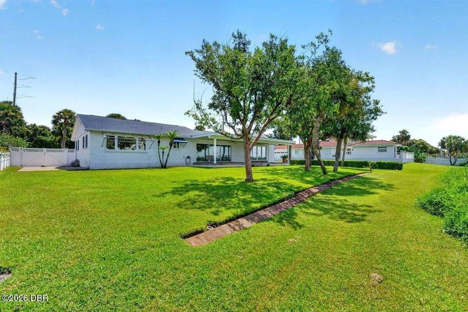 A white, single-story house with a large lawn and mature trees under a blue sky — 448 RIVERSIDE DRIVE, ORMOND BEACH, FL