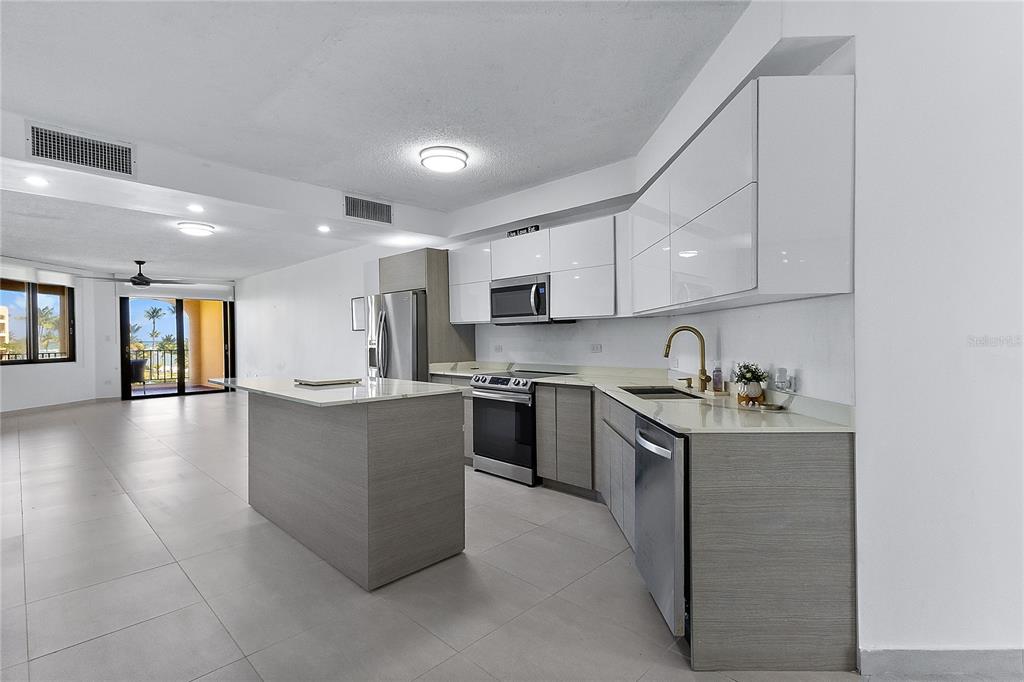 A modern kitchen features white upper cabinets, wood-tone lower cabinets, stainless steel appliances, and an island — 190 CANDELERO DRIVE UNIT 175, HUMACAO, PR