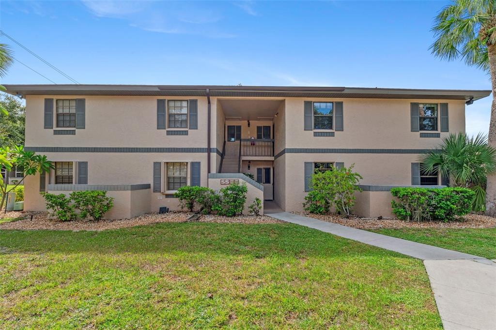 A two-story apartment building with beige stucco walls, dark shutters, and a central stairwell — 19505 QUESADA AVENUE UNIT SS201, PORT CHARLOTTE, FL