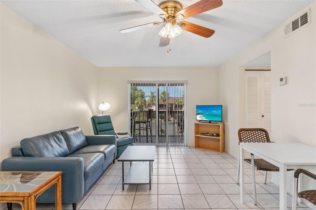 A living room with tile flooring, a blue sofa, a ceiling fan, and sliding glass doors — 19505 QUESADA AVENUE UNIT SS201, PORT CHARLOTTE, FL