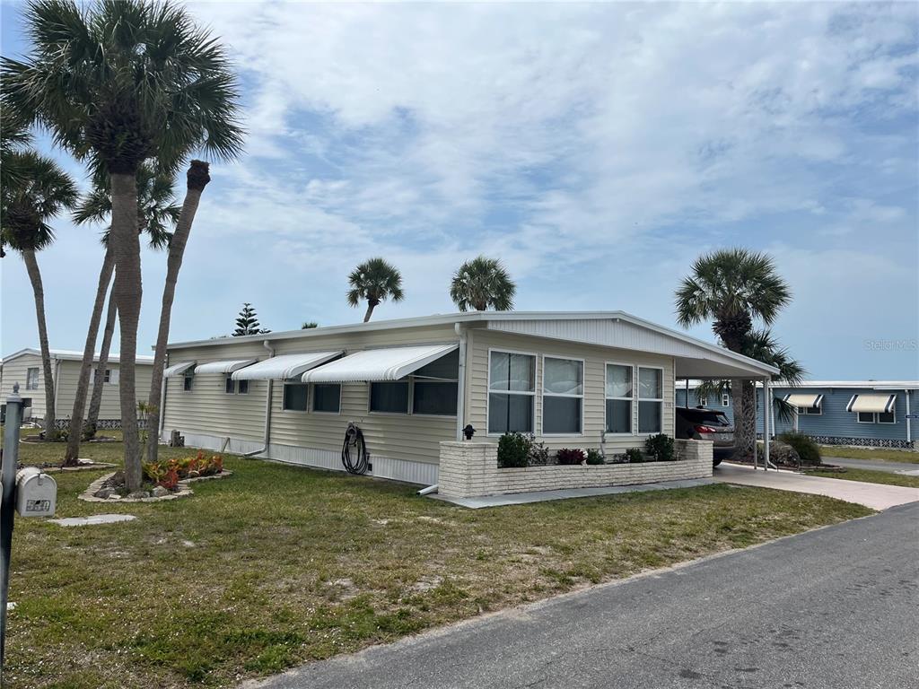 A light-colored mobile home features a brick planter, metal awnings, and palm trees — 530 VIA VENETO, VENICE, FL
