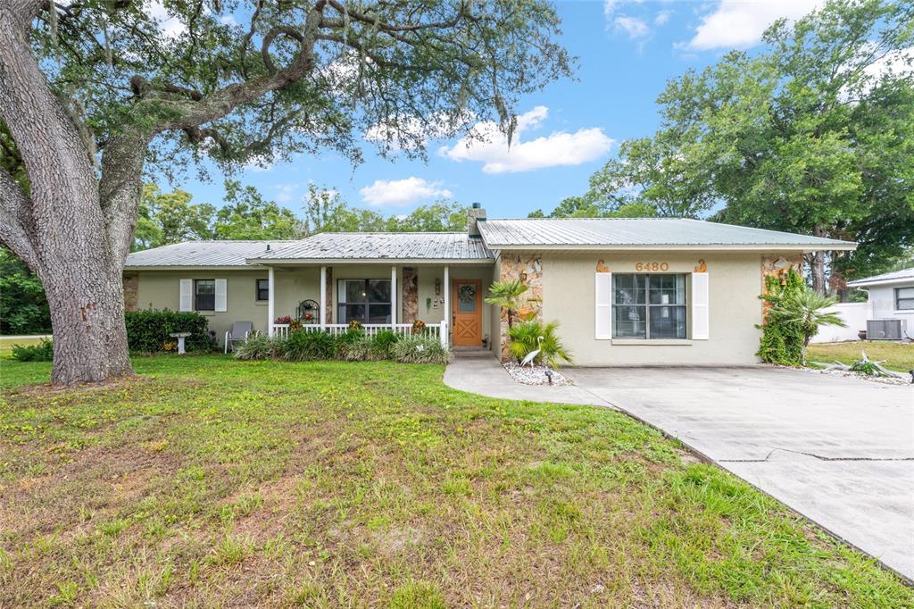 A single-story house with a metal roof, stone accents, and a large tree in front — 6480 SE 42ND COURT, OCALA, FL