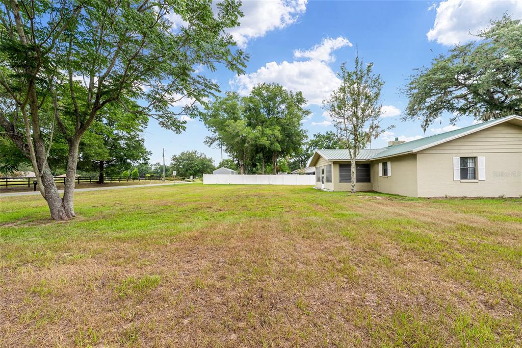 A grassy yard extends toward a tan house with a screened porch and white fence — 6480 SE 42ND COURT, OCALA, FL