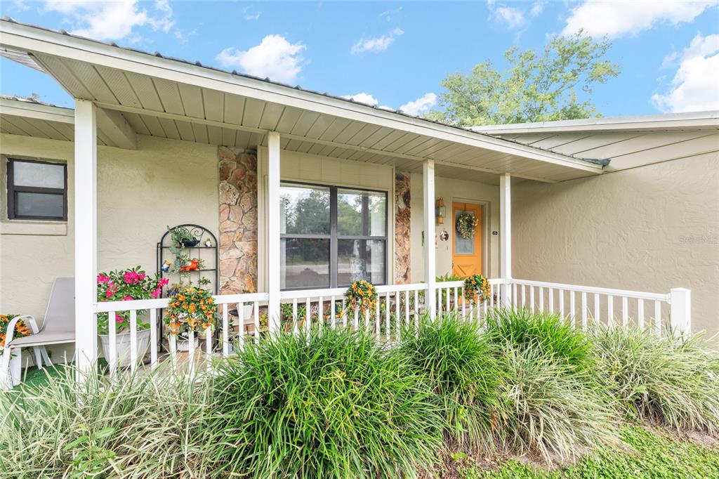 A covered front porch features a white railing, stone accents, and a yellow front door — 6480 SE 42ND COURT, OCALA, FL