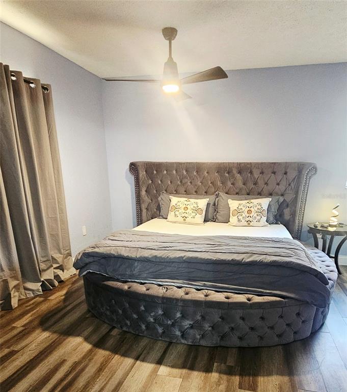 A bedroom features a tufted circular bed, wood-look flooring, and a ceiling fan — 7714 DELEUIL AVENUE, TAMPA, FL