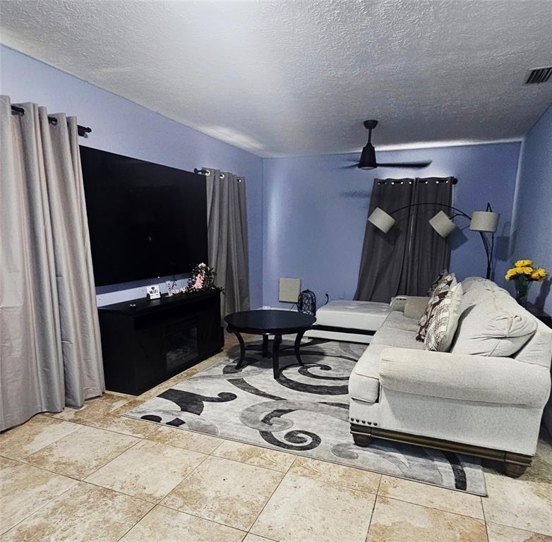 A living room features light blue walls, tile flooring, a large television, and a sectional sofa — 7714 DELEUIL AVENUE, TAMPA, FL