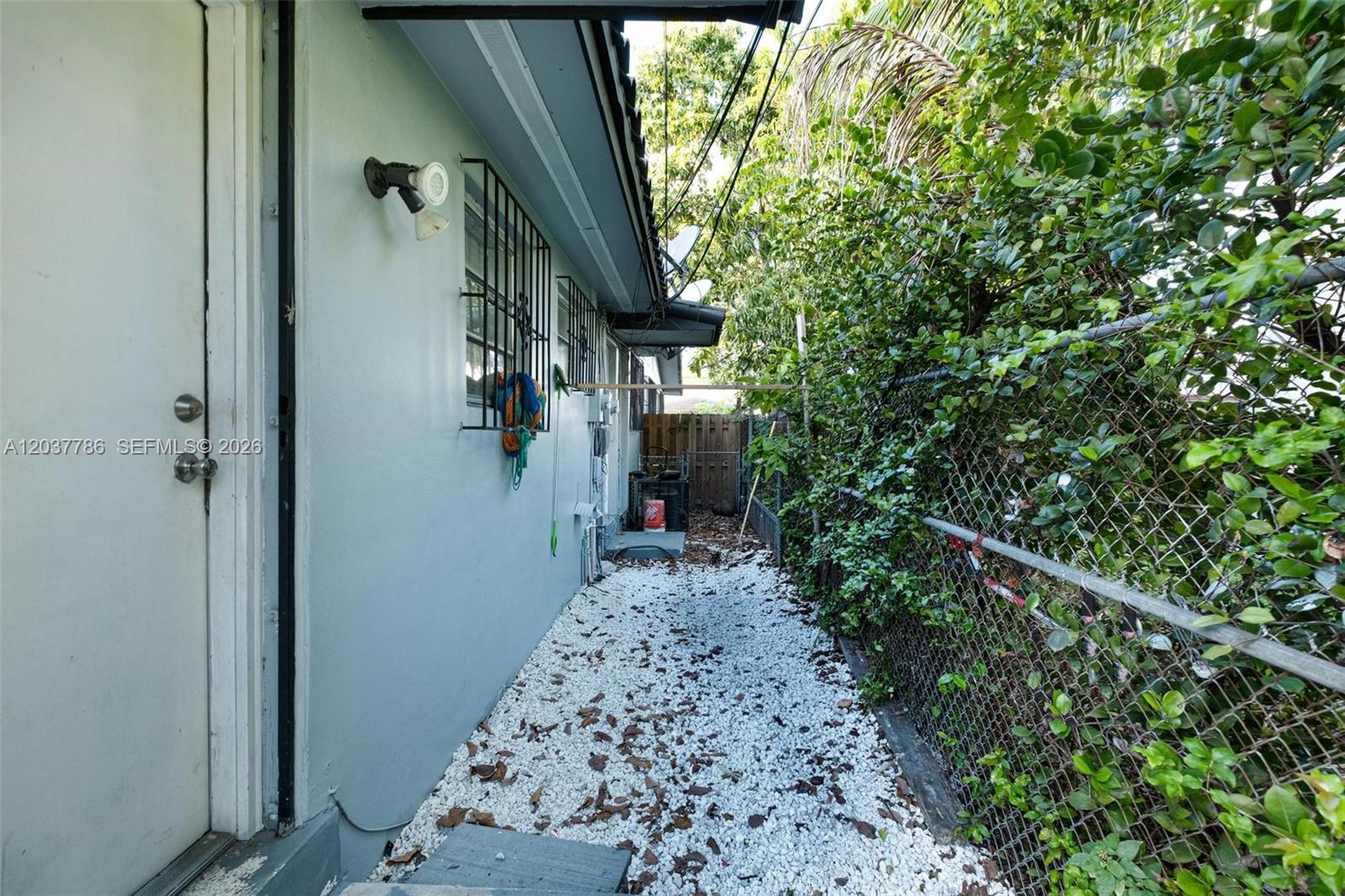 A narrow side yard features white gravel, a chain-link fence, and a light-colored house wall — 1519 NW 40th St # 1, Miami FL 33142, MIAMI, FL