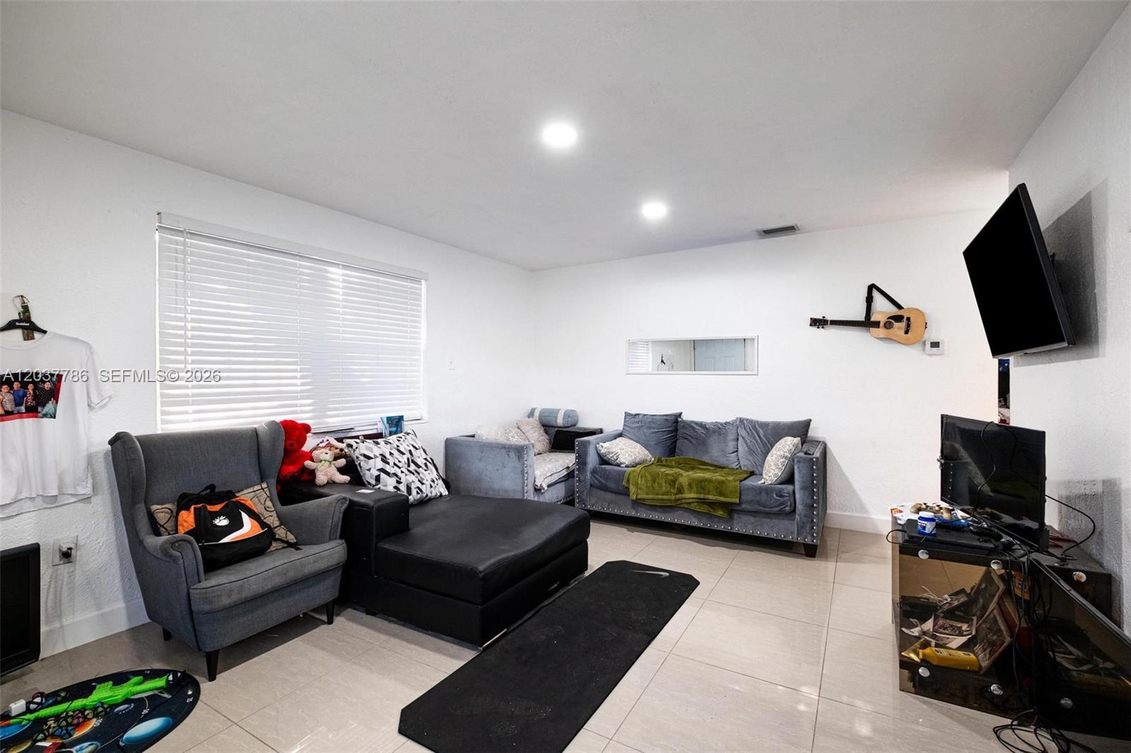 A living room features a gray sofa, a black chaise lounge, and a wall-mounted guitar — 1519 NW 40th St # 1, Miami FL 33142, MIAMI, FL
