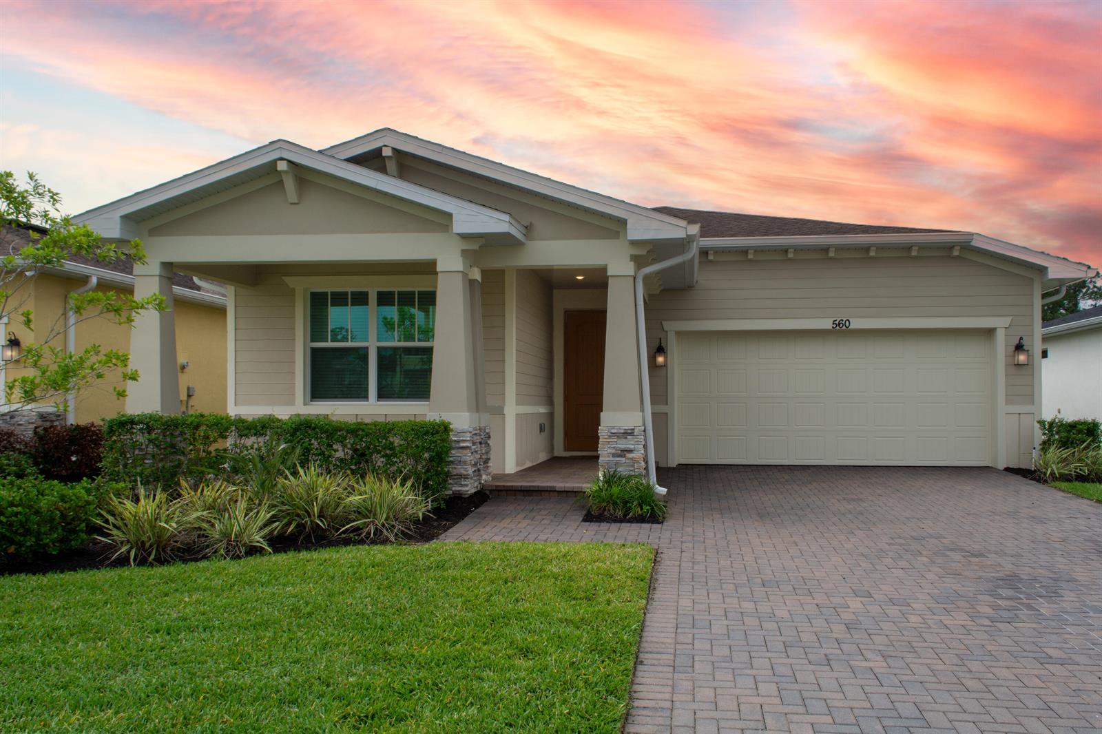 A single-story house with beige siding, a stone-accented porch, and a paved driveway at sunset — 560 Veridian Circle NW, Palm Bay FL 32907, PALM BAY, FL