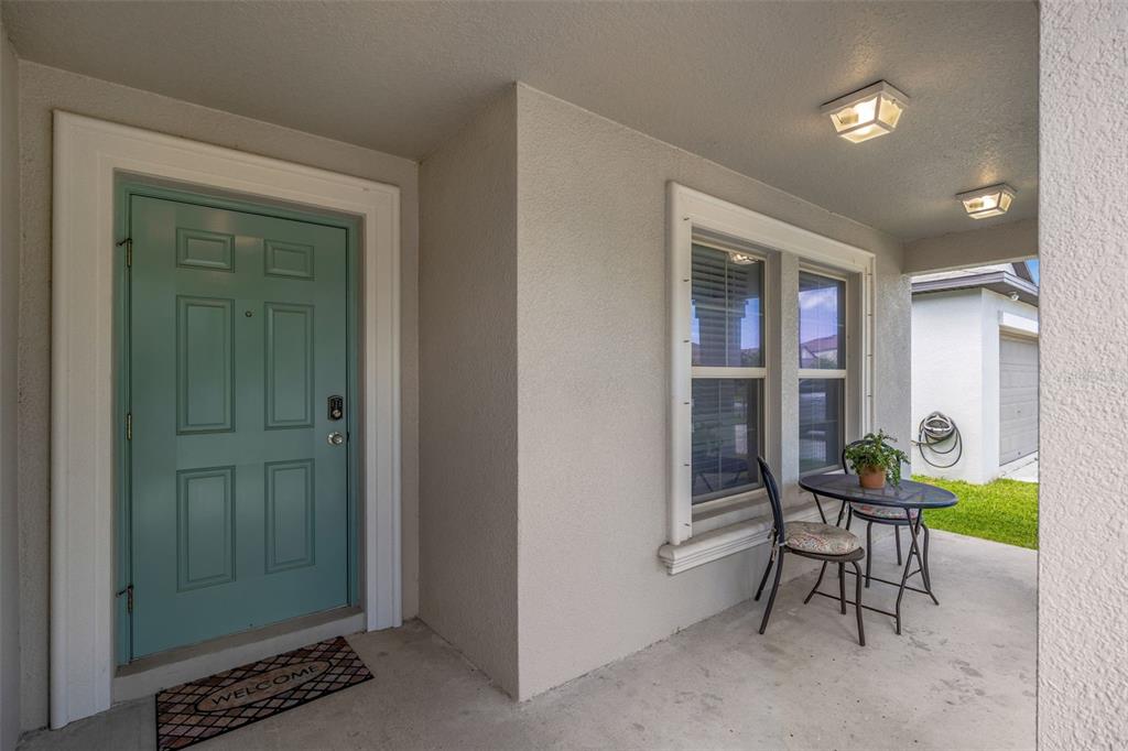 A covered front porch features a teal door, a small bistro set, and two lights — 138 RAIN BERRY AVENUE, RUSKIN, FL