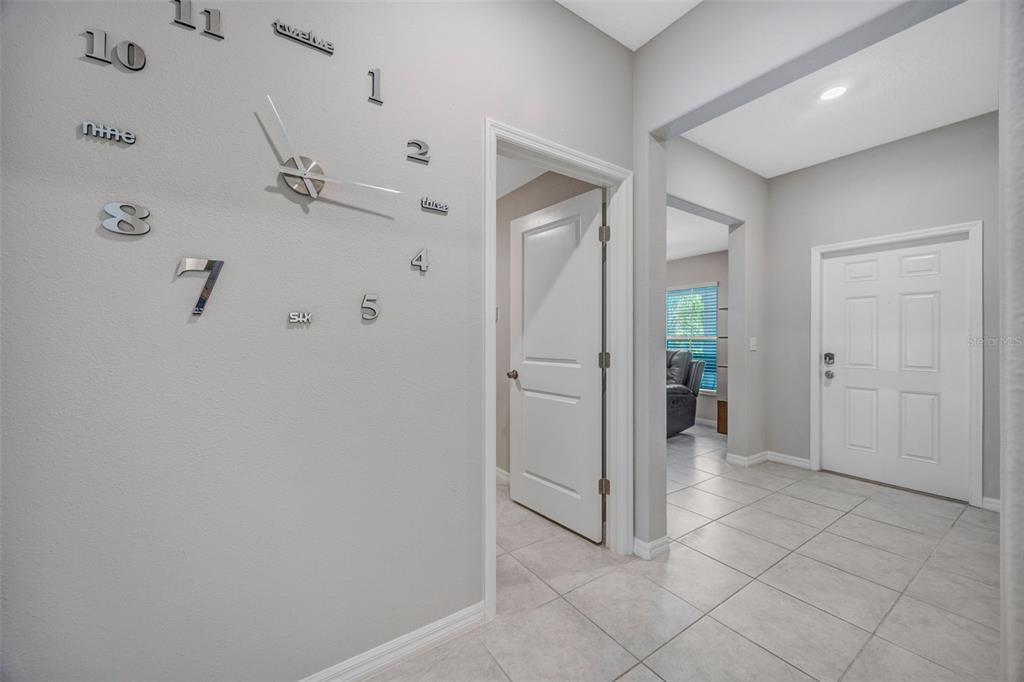 A tiled entryway features a large wall-mounted clock and a white door leading to another room — 138 RAIN BERRY AVENUE, RUSKIN, FL
