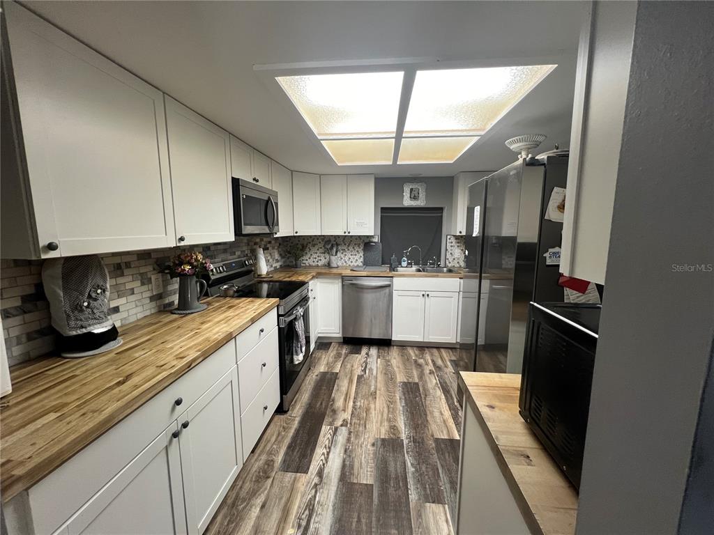 A kitchen features white cabinets, butcher block countertops, stainless steel appliances, and wood-look flooring — 220 NE 11TH STREET, CRYSTAL RIVER, FL