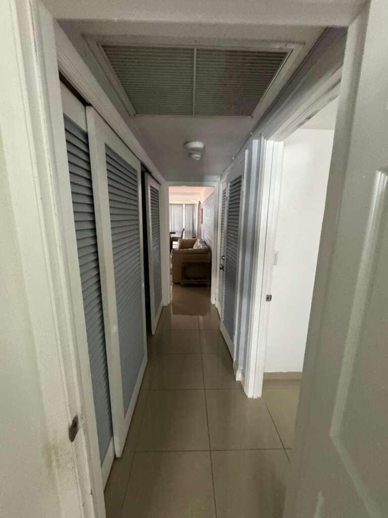 A hallway with light-colored tile flooring, louvered closet doors, and a view into a living area — 1001 S Riverside Drive # 104, Pompano Beach FL 33062, POMPANO BEACH, FL