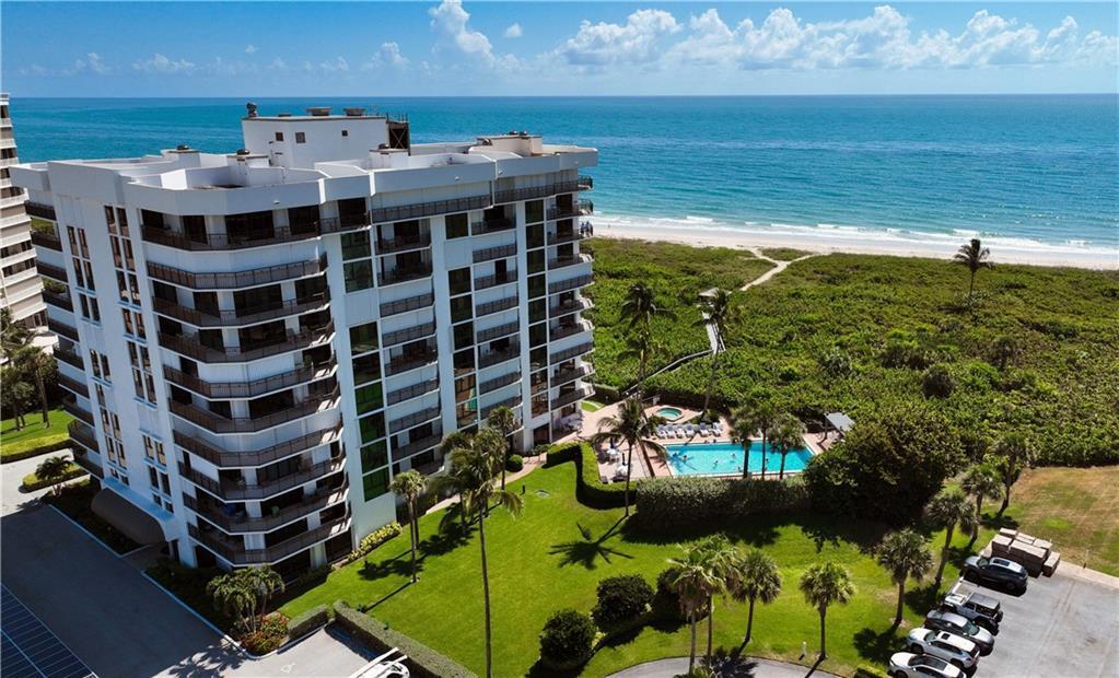 An aerial view shows a multi-story beachfront condominium building with a pool and parking lot — HUTCHINSON ISLAND, FL