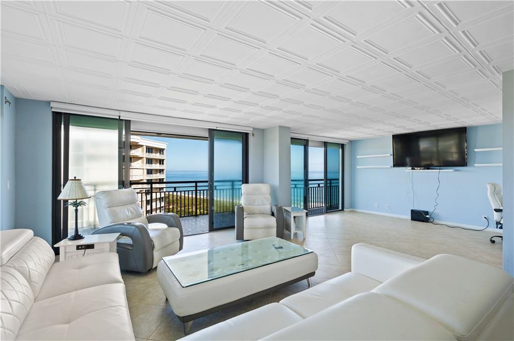 A living room with white leather furniture, a glass coffee table, and ocean views — HUTCHINSON ISLAND, FL