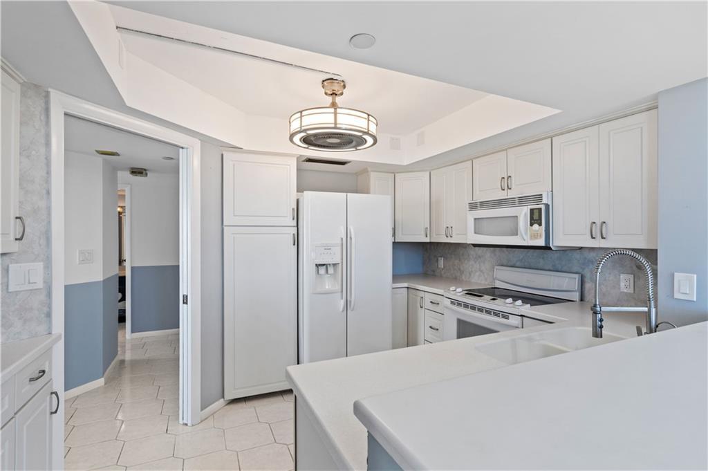 A kitchen with white cabinets, white appliances, and a breakfast bar overlooking a tiled floor — HUTCHINSON ISLAND, FL