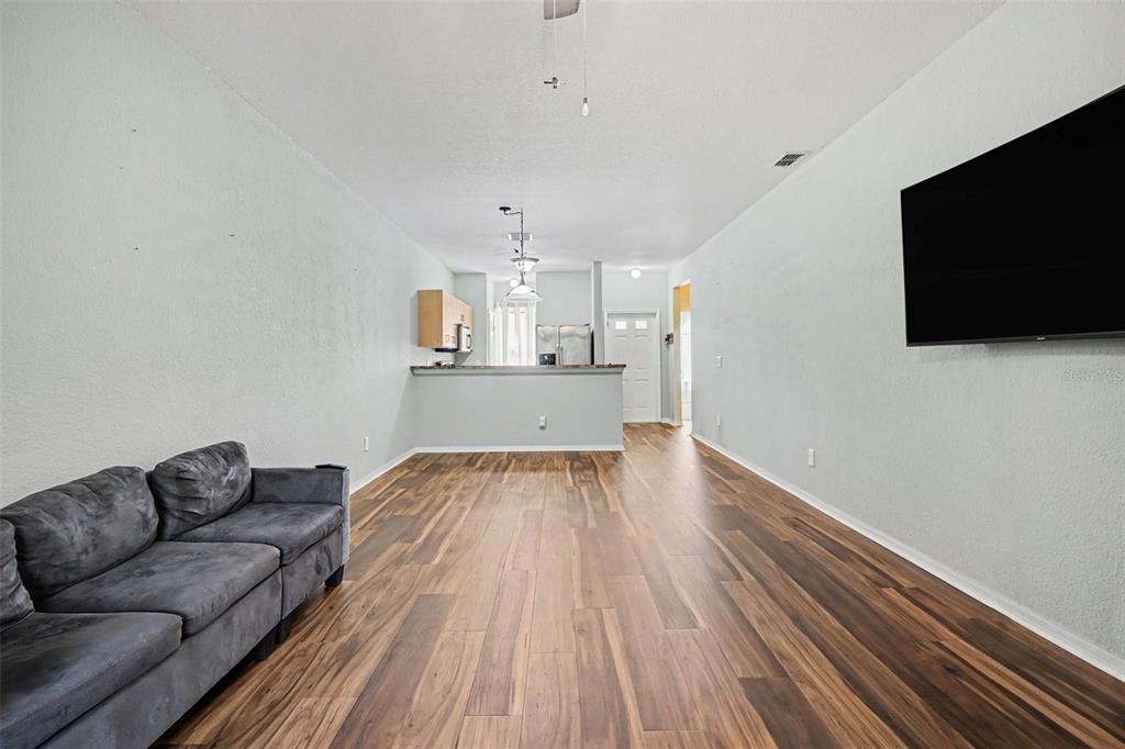 A living room with wood-look flooring, a grey sofa, and a wall-mounted television — 12202 INDIAN CREEK DRIVE, KISSIMMEE, FL