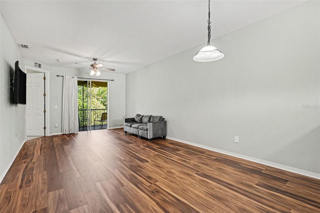 A living room features wood-look flooring, a grey sofa, a ceiling fan, and a balcony — 12202 INDIAN CREEK DRIVE, KISSIMMEE, FL