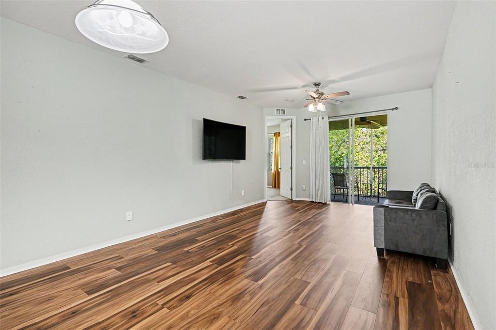 A living room features wood-look flooring, a wall-mounted television, a ceiling fan, and a balcony — 12202 INDIAN CREEK DRIVE, KISSIMMEE, FL