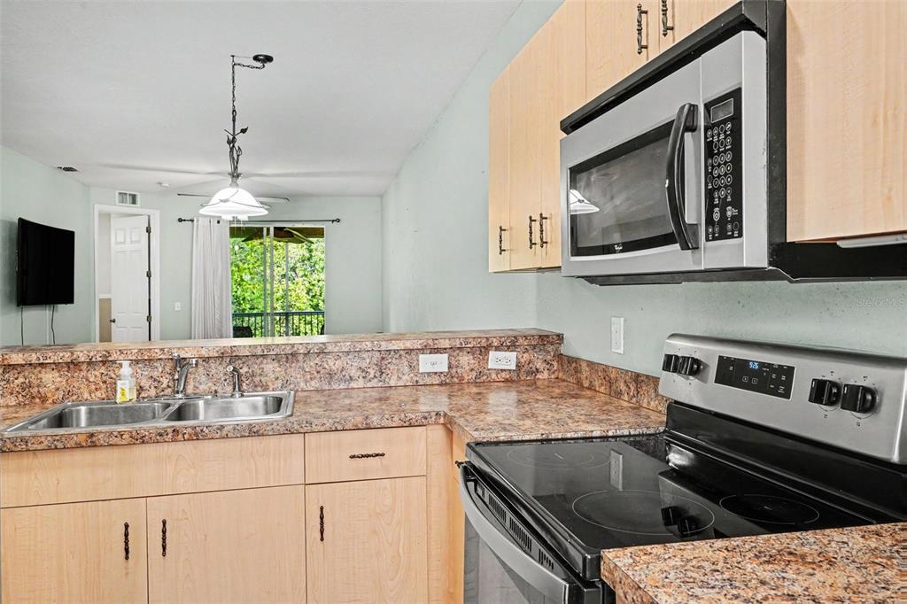 A kitchen features light wood cabinets, granite countertops, a stainless steel stove, and a microwave — 12202 INDIAN CREEK DRIVE, KISSIMMEE, FL