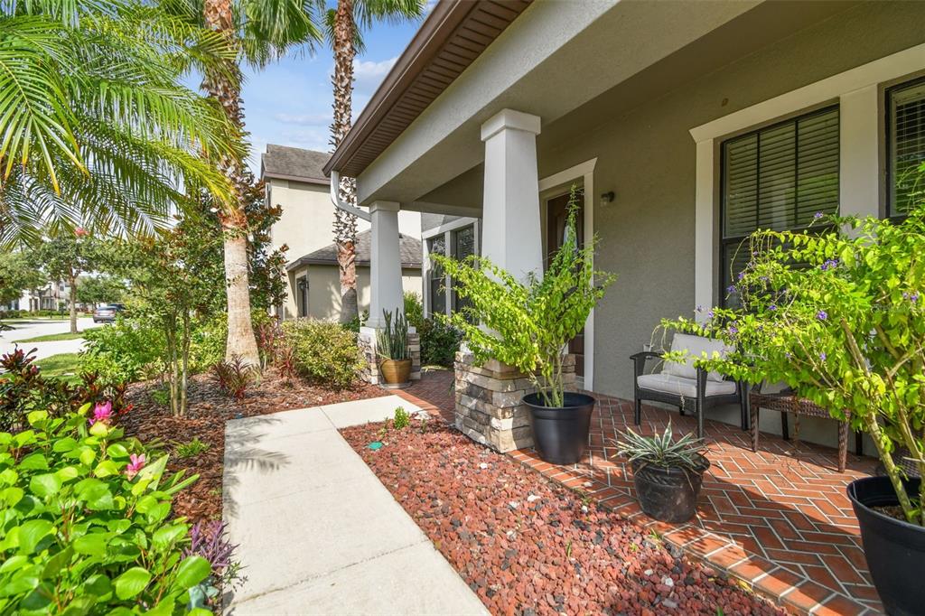 A front porch with a herringbone brick floor, white columns, and potted plants — 10627 MISTFLOWER LANE, TAMPA, FL