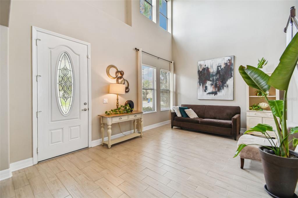 A bright entryway features high ceilings, light wood-look tile flooring, a sofa, and a console table — 10627 MISTFLOWER LANE, TAMPA, FL