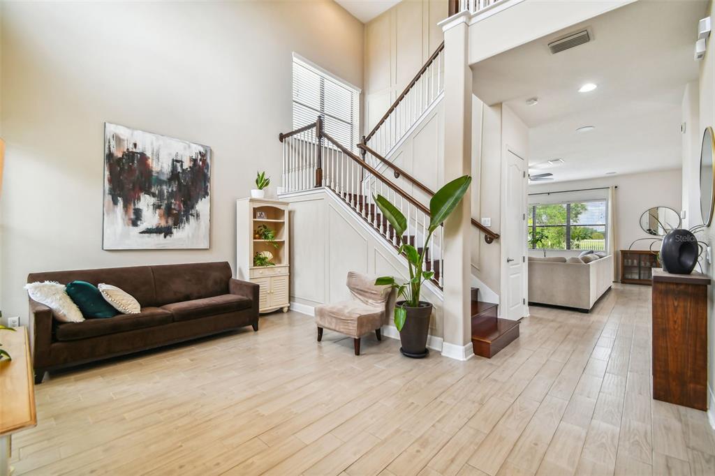 A living room features a brown sofa, a staircase, and light wood-look tile flooring — 10627 MISTFLOWER LANE, TAMPA, FL