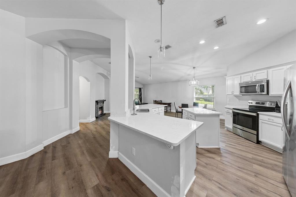 A bright kitchen features white cabinetry, quartz countertops, a center island, and wood-look flooring — 1365 SHOOTINGSTAR LANE, ST JOHNS, FL