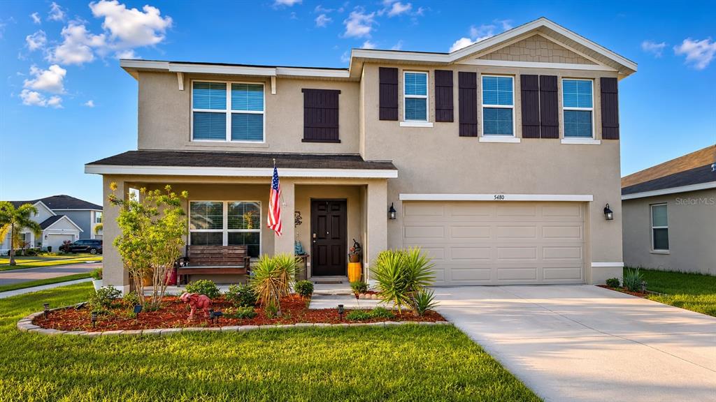 A two-story suburban house with a beige stucco exterior, a front porch, and a garage — 5480 LOGAN CAVE AVENUE, WIMAUMA, FL
