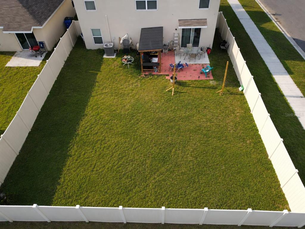An aerial view shows a fenced backyard with a patio, a small structure, and grass — 5480 LOGAN CAVE AVENUE, WIMAUMA, FL
