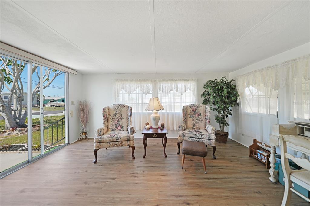 A sunroom features wood-look flooring, two floral armchairs, a side table, and sliding glass doors — 1407 SEAGULL DRIVE, ENGLEWOOD, FL