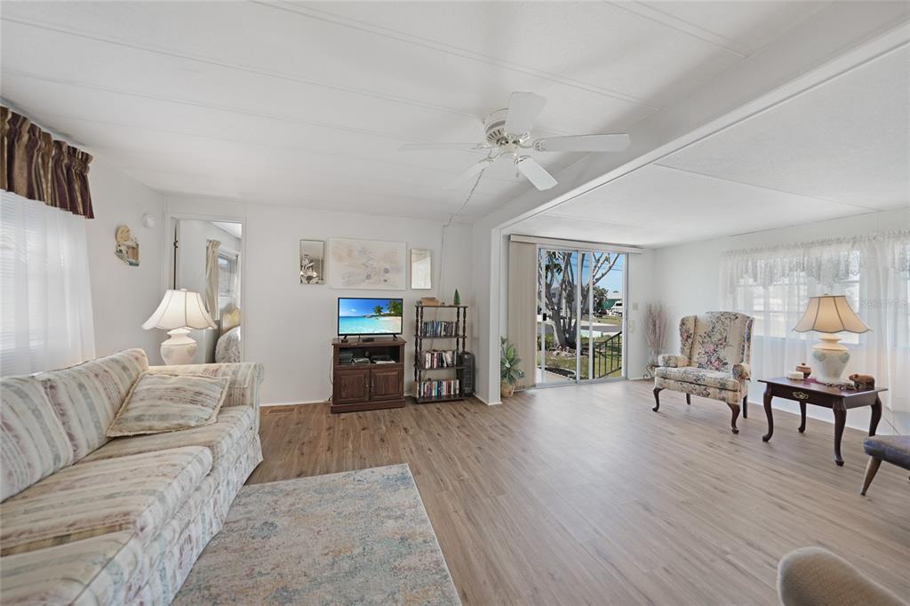 A living room features light wood-look flooring, a ceiling fan, and a sliding glass door — 1407 SEAGULL DRIVE, ENGLEWOOD, FL