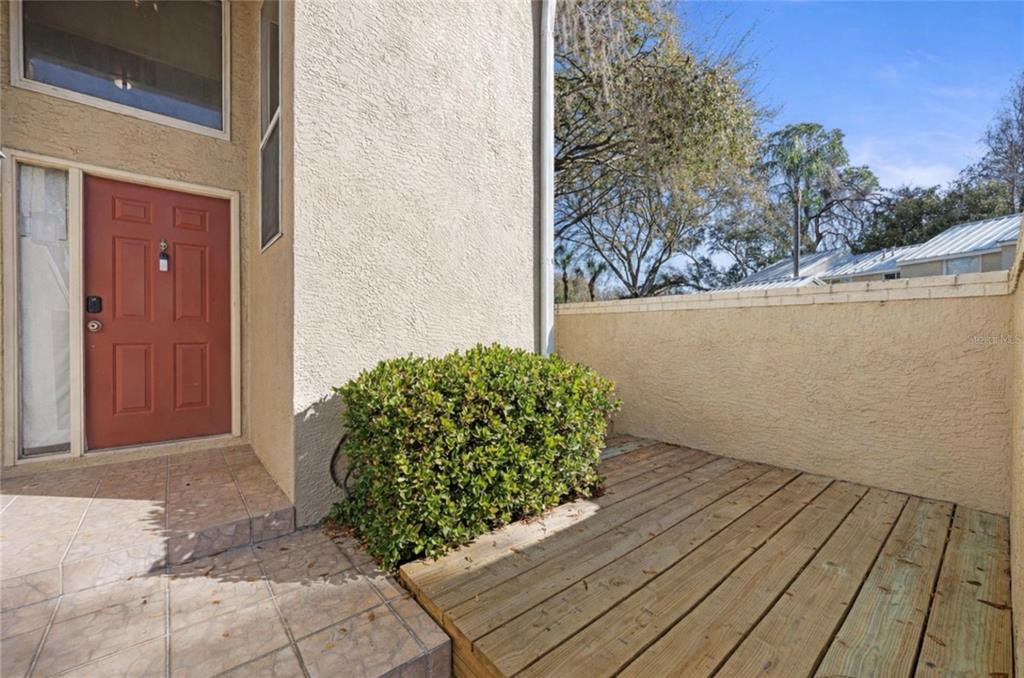 A red front door opens onto a tiled entryway next to a wooden deck area — 3401 CYPRESS HEAD COURT, TAMPA, FL