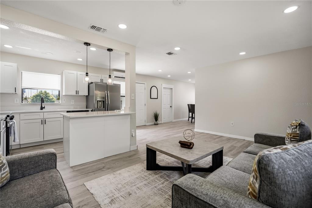 An open-concept living room and kitchen featuring white cabinets, gray sofas, and light flooring — 2601 HEALY DRIVE, ORLANDO, FL
