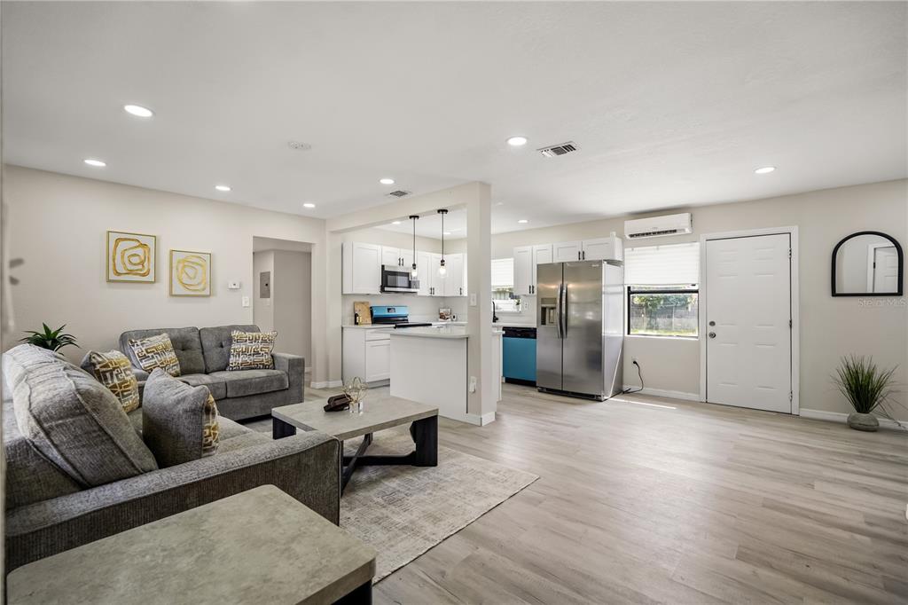 An open-concept living room and kitchen featuring gray flooring, white cabinetry, and stainless steel appliances — 2601 HEALY DRIVE, ORLANDO, FL