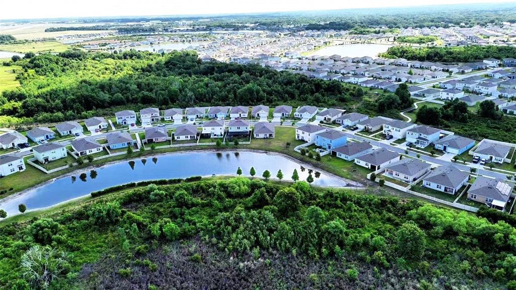 An aerial view shows a suburban neighborhood with houses surrounding a small retention pond — 5567 SILTSTONE STREET, LAKELAND, FL