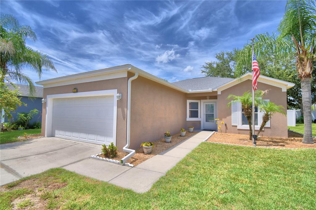 A single-story tan house with a white garage door, a front walkway, and a flagpole — 5621 FOREST RIDGE DRIVE, WINTER HAVEN, FL