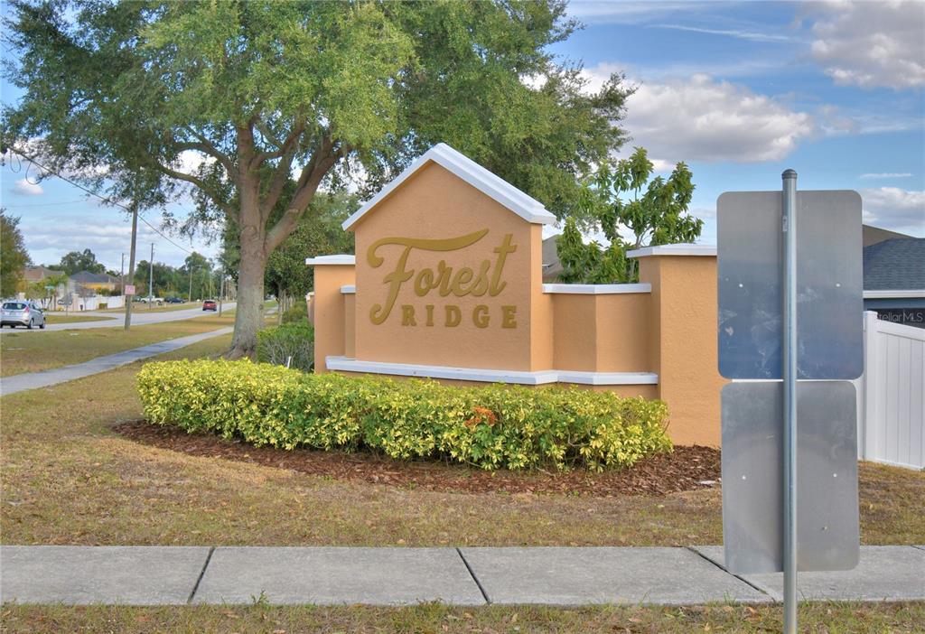 A tan stucco monument sign for Forest Ridge sits in a landscaped yard near a road — 5621 FOREST RIDGE DRIVE, WINTER HAVEN, FL