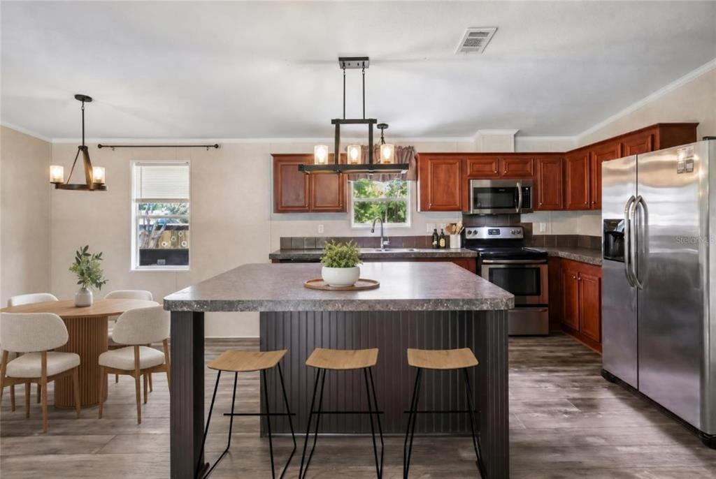 A kitchen with wood cabinets, a large island with bar seating, and an adjacent dining area — 136 CREEKWOOD RUN, LAKELAND, FL