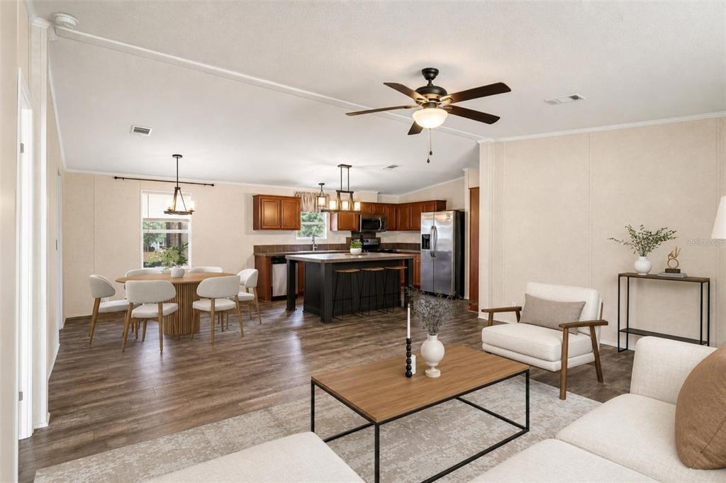 An open-concept living, dining, and kitchen area features wood-look flooring, a kitchen island, and neutral walls — 136 CREEKWOOD RUN, LAKELAND, FL
